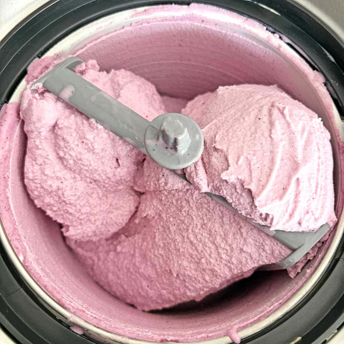 Pink strawberry ice cream in a freezer tub with a metal scoop.