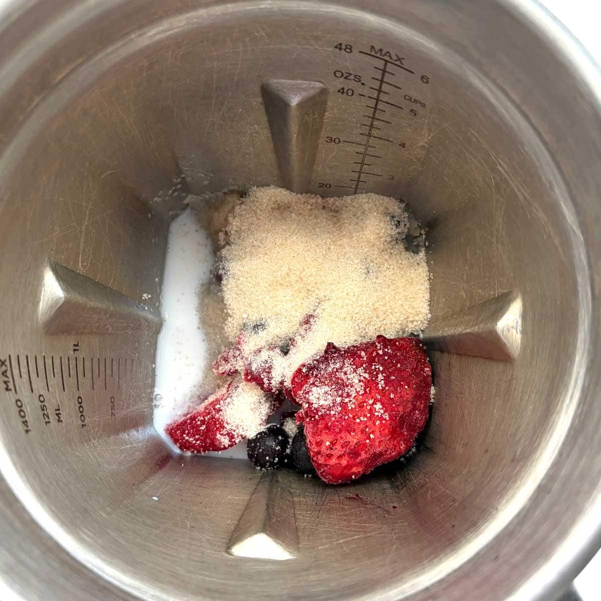 Mixed berries with sugar and milk in blender.