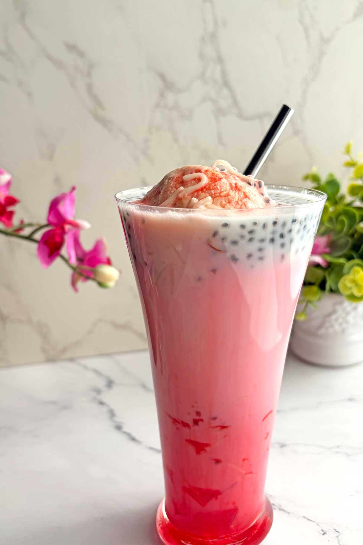 Tall pink bubble tea with black tapioca pearls, topped by a scoop of pink ice cream and a striped straw in a tall glass