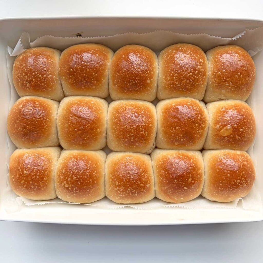 Sourdough dinner rolls brushed with butter in a white tray.